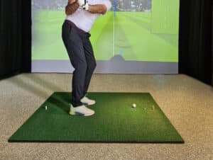 Professional male golfer holding club playing golf indoors on golf simulator